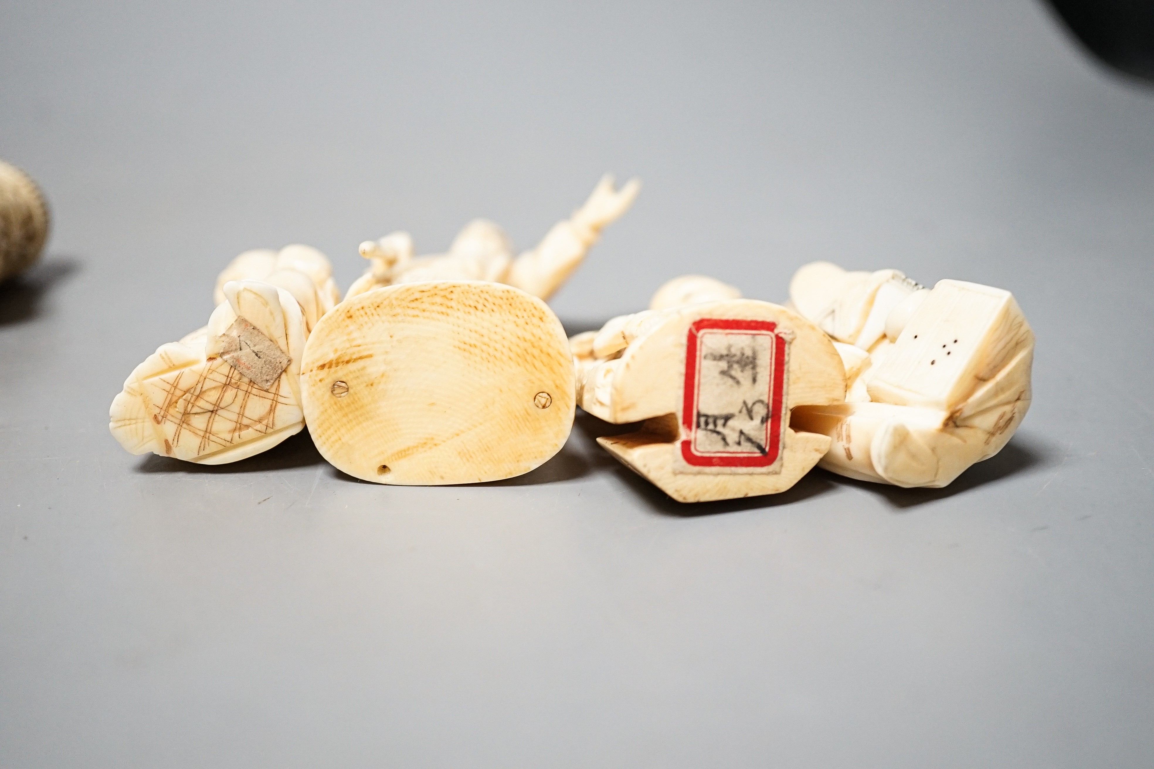 Three Japanese Ivory figures of men, a similar bezique marker, a Japanese staghorn single section inro with ivory manju, a Chinese ivory carving and a bone needlework container